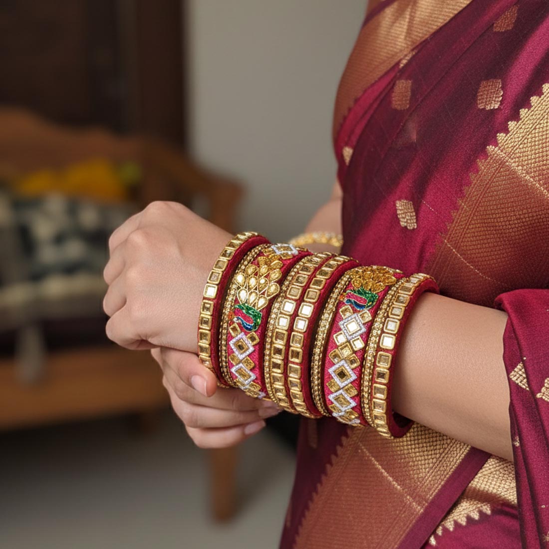 A royal maroon bridal bangle set wrapped in premium silk thread, beautifully decorated with gold-toned stone frames, geometric diamond rhinestone layouts, and dual enameled green and blue peacock motifs on a cream-colored silk backdrop.