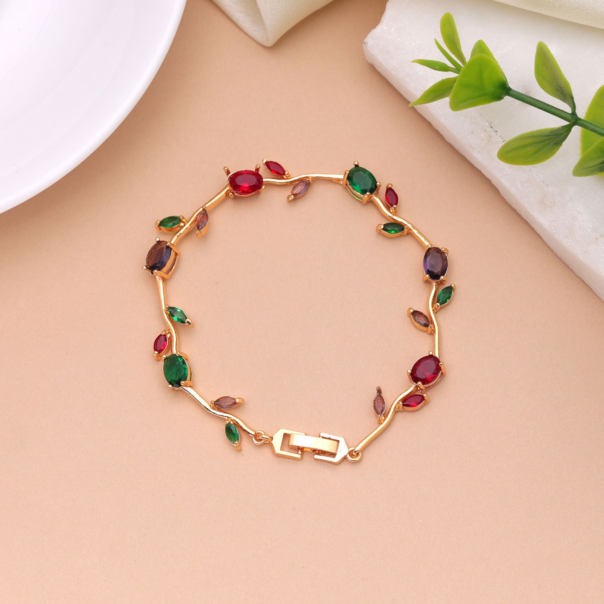 A delicate gold-plated chain bracelet featuring an organic vine and leaf branch design embedded with multi-color oval and marquise-cut cubic zirconia stones secured with a polished watch-band foldover clasp.