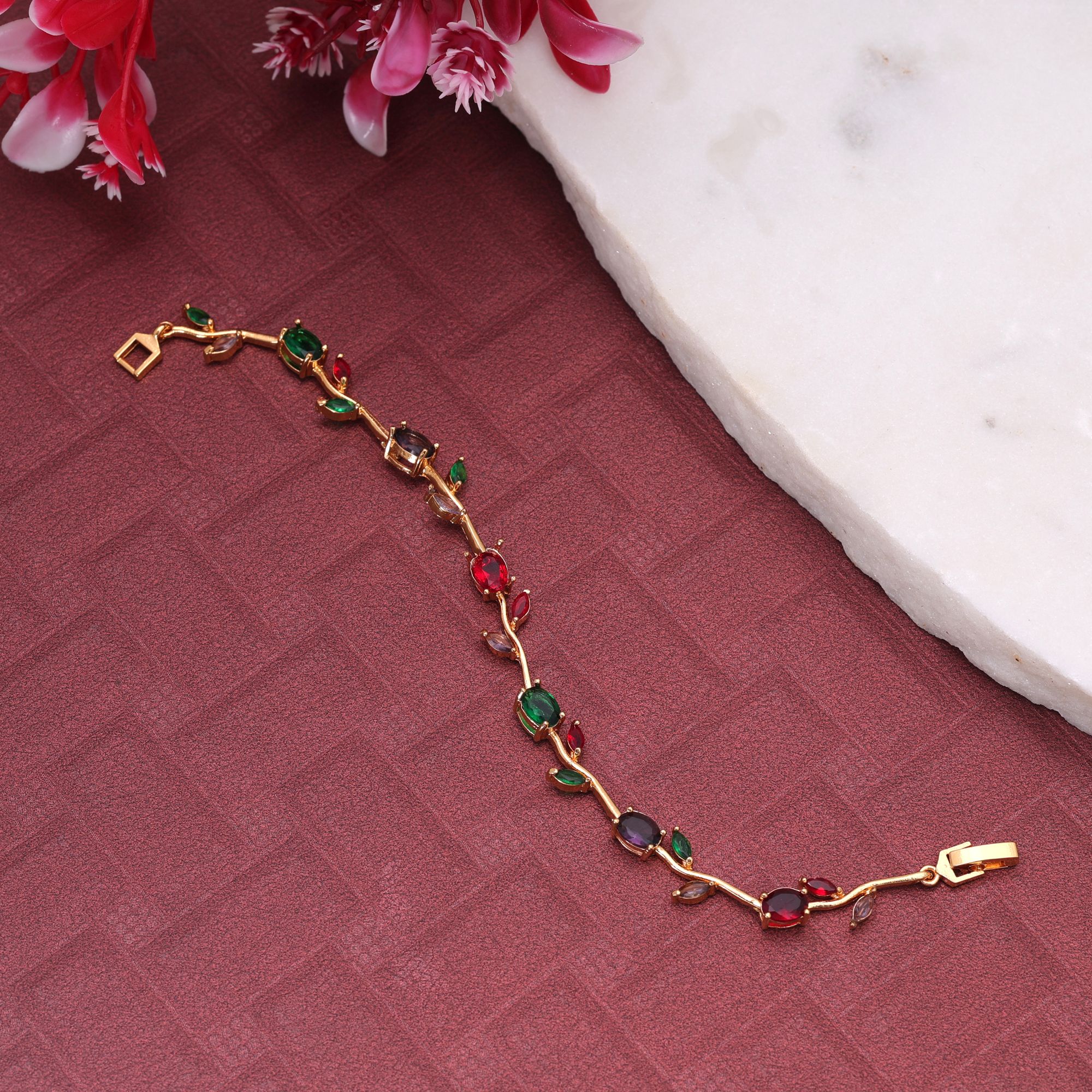 A delicate gold-plated chain bracelet featuring an organic vine and leaf branch design embedded with multi-color oval and marquise-cut cubic zirconia stones secured with a polished watch-band foldover clasp.