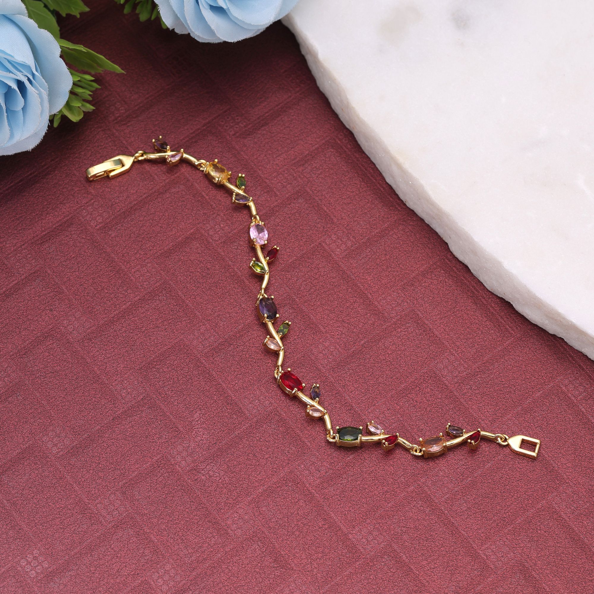 A delicate gold-plated chain bracelet featuring an organic vine and leaf branch design embedded with multi-color oval and marquise-cut cubic zirconia stones secured with a polished watch-band foldover clasp.