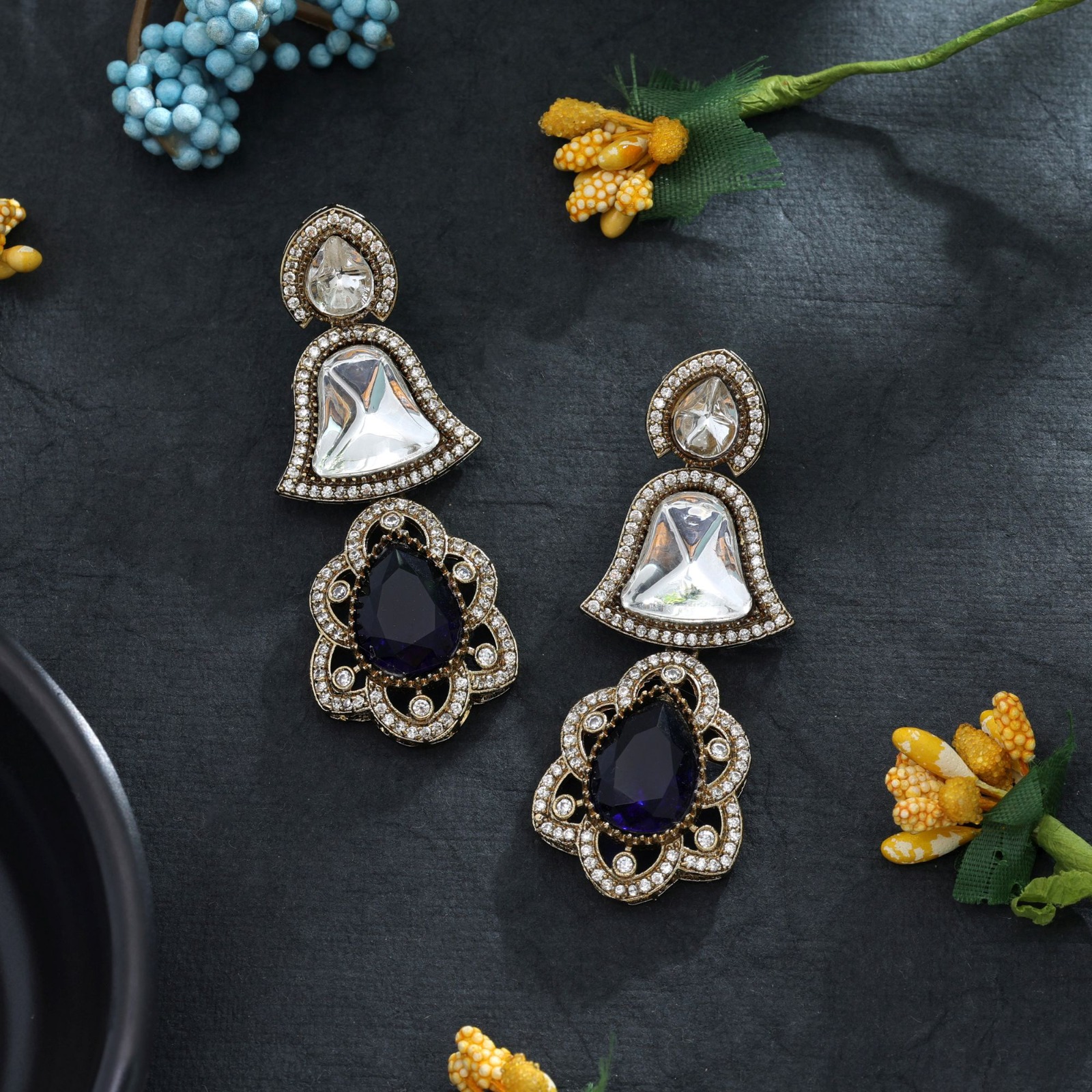 Statement drop earrings featuring bell-shaped clear accents, deep sapphire-blue Monalisa stone teardrop pendants, and a micro-pave American Diamond halo.