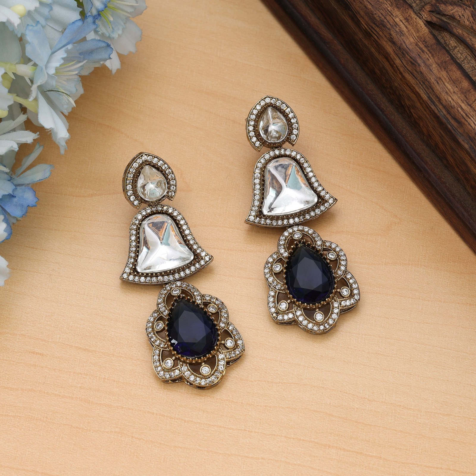 Statement drop earrings featuring bell-shaped clear accents, deep sapphire-blue Monalisa stone teardrop pendants, and a micro-pave American Diamond halo.