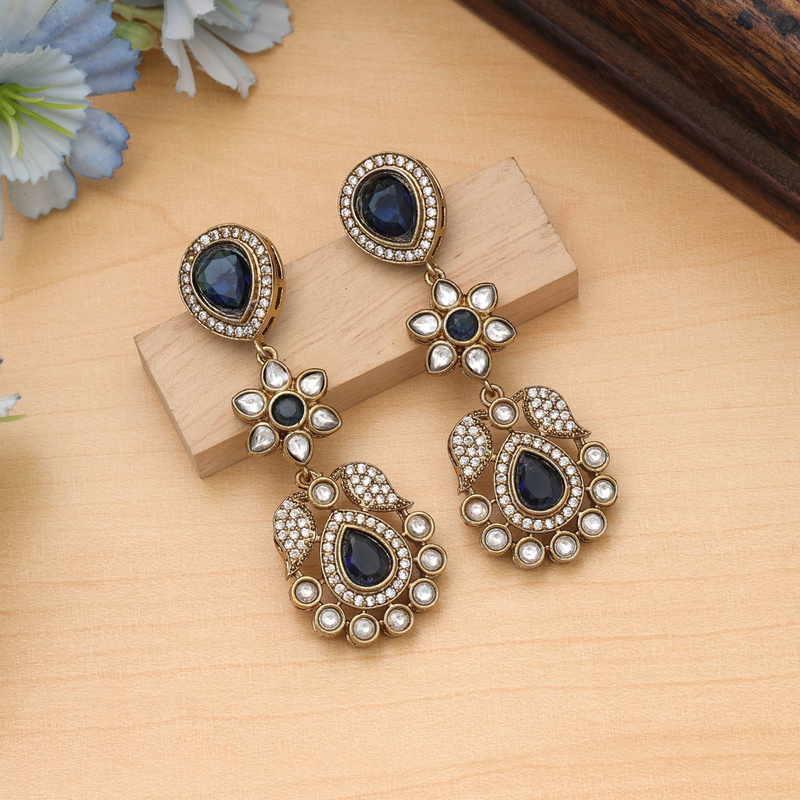 Pair of antique gold drop earrings with teardrop royal blue Monalisa stones, floral Kundan motifs, and sparkling American Diamond micro-pave borders.