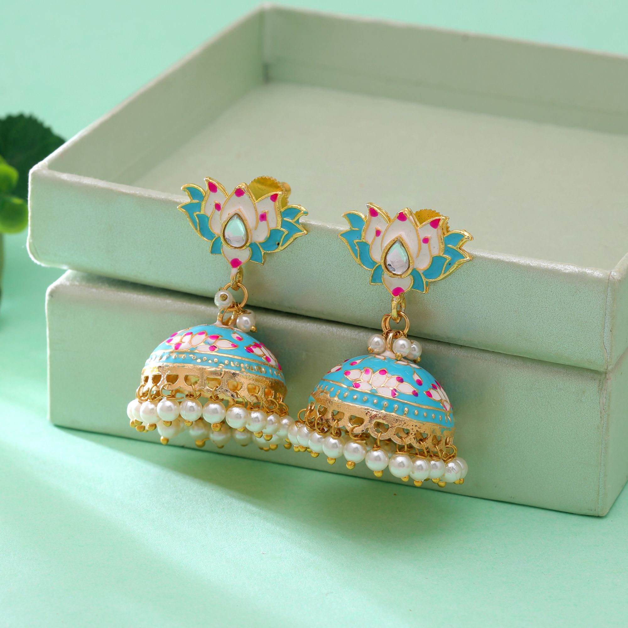 A pair of traditional gold-plated sky blue Meenakari jhumka earrings featuring an upper stud shaped like a blooming lotus flower with white and pink petals, a bell-shaped dome detailed with lotus blossoms and gold vines, and a lower fringe of dangling white faux pearl drops.