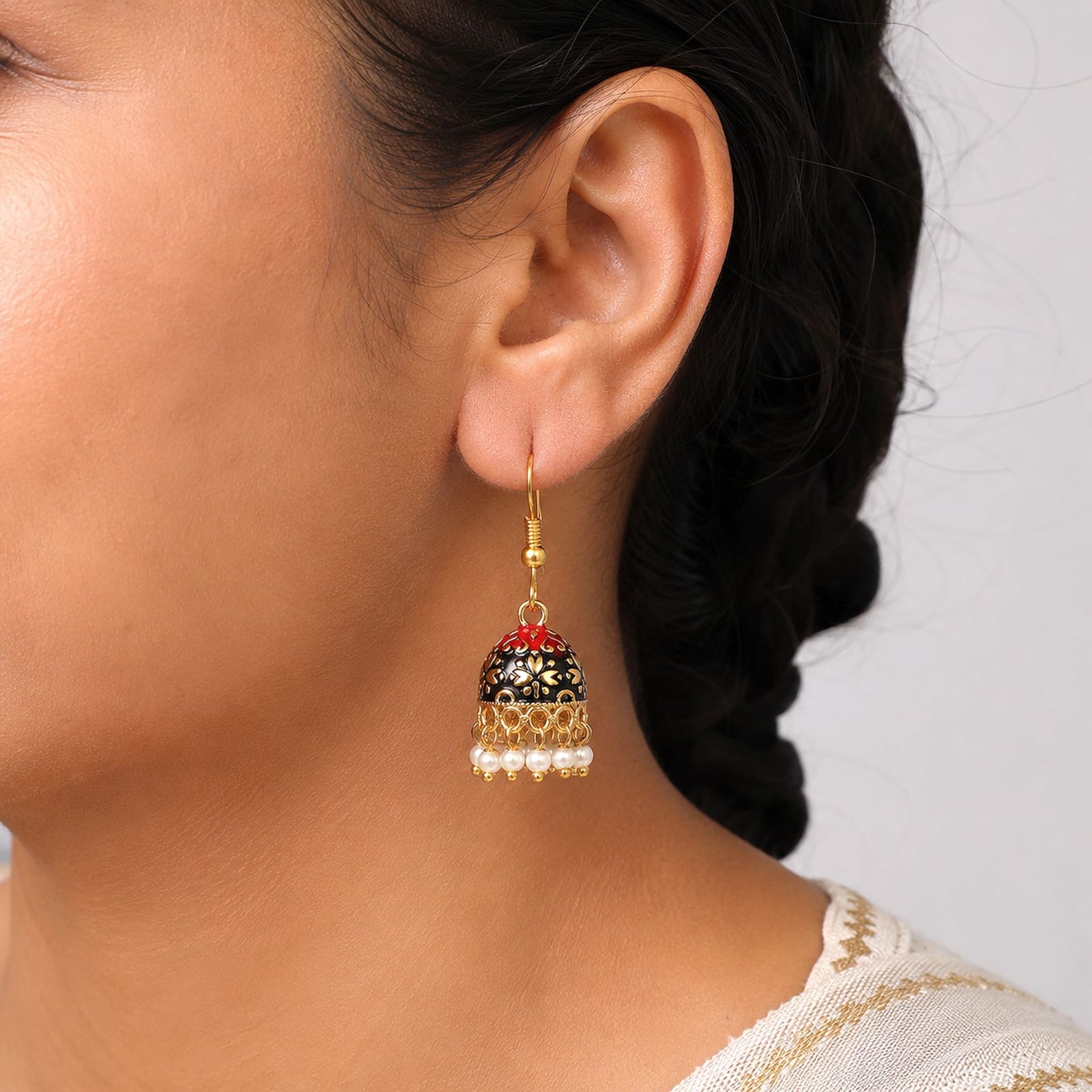 Add a touch of traditional charm to your ensemble with these gold-toned mini Meenakari jhumkas. Crafted with intricate enamel work, the bell-shaped dome highlights a vibrant dual-tone design of Maroon at the top and Black at the base, detailed with intricate gold floral patterns. A delicate fringe of faux pearl drops along the bottom rim adds playful movement and elegance. Lightweight and fitted with classic French fish-hook closures, these earrings are perfect for festive occasions, ethnic celebrations, or elevating everyday traditional attire.