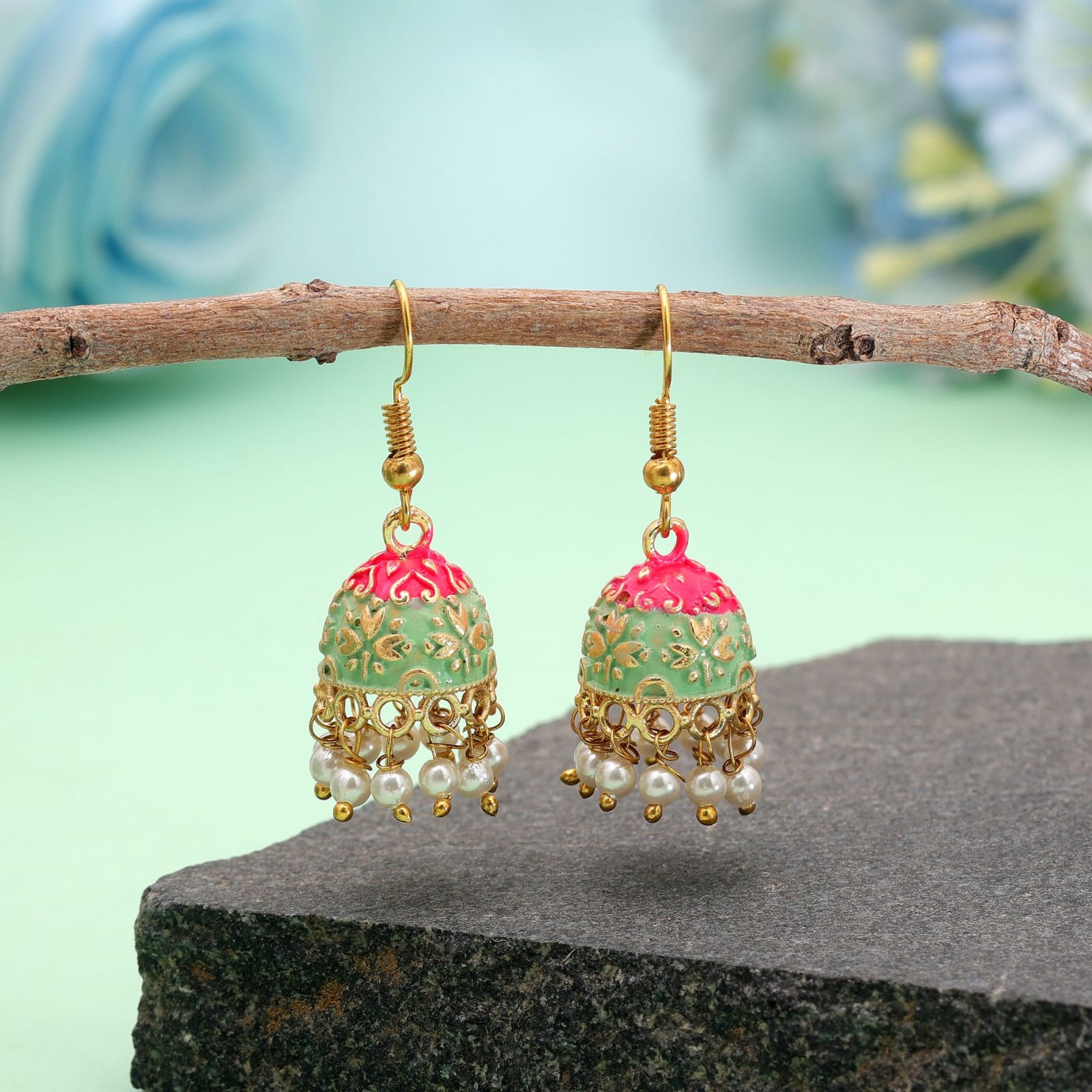 Add a touch of traditional charm to your ensemble with these gold-toned mini Meenakari jhumkas. Crafted with intricate enamel work, the bell-shaped dome highlights a vibrant dual-tone design of bright pink at the top and light mint green at the base, detailed with intricate gold floral patterns. A delicate fringe of faux pearl drops along the bottom rim adds playful movement and elegance. Lightweight and fitted with classic French fish-hook closures, these earrings are perfect for festive occasions, ethnic celebrations, or elevating everyday traditional attire.