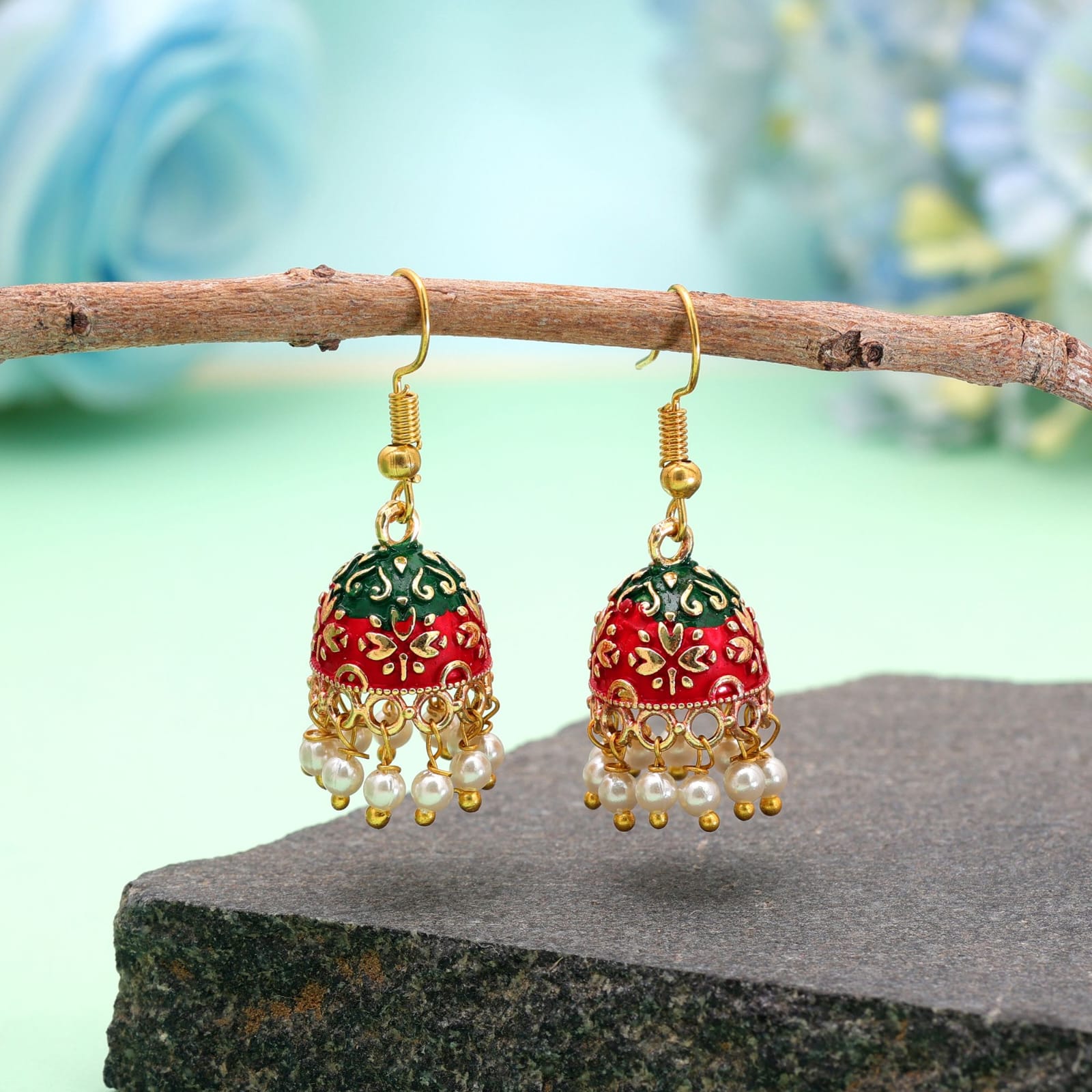 Add a touch of traditional charm to your ensemble with these gold-toned mini Meenakari jhumkas. Crafted with intricate enamel work, the bell-shaped dome highlights a vibrant dual-tone design of bright red at the top and green at the base, detailed with intricate gold floral patterns. A delicate fringe of faux pearl drops along the bottom rim adds playful movement and elegance. Lightweight and fitted with classic French fish-hook closures, these earrings are perfect for festive occasions, ethnic celebrations, or elevating everyday traditional attire.