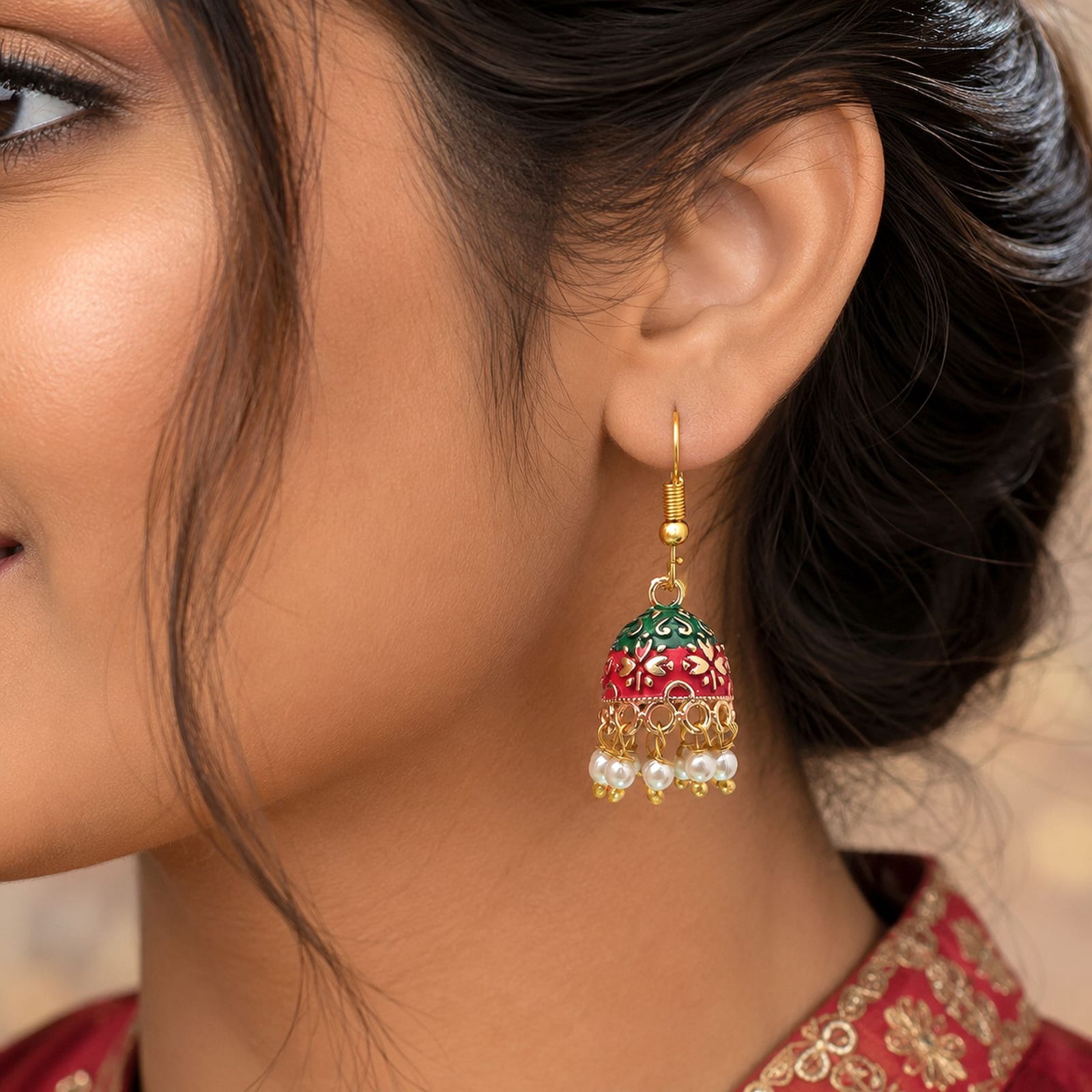 Add a touch of traditional charm to your ensemble with these gold-toned mini Meenakari jhumkas. Crafted with intricate enamel work, the bell-shaped dome highlights a vibrant dual-tone design of bright red at the top and green at the base, detailed with intricate gold floral patterns. A delicate fringe of faux pearl drops along the bottom rim adds playful movement and elegance. Lightweight and fitted with classic French fish-hook closures, these earrings are perfect for festive occasions, ethnic celebrations, or elevating everyday traditional attire.