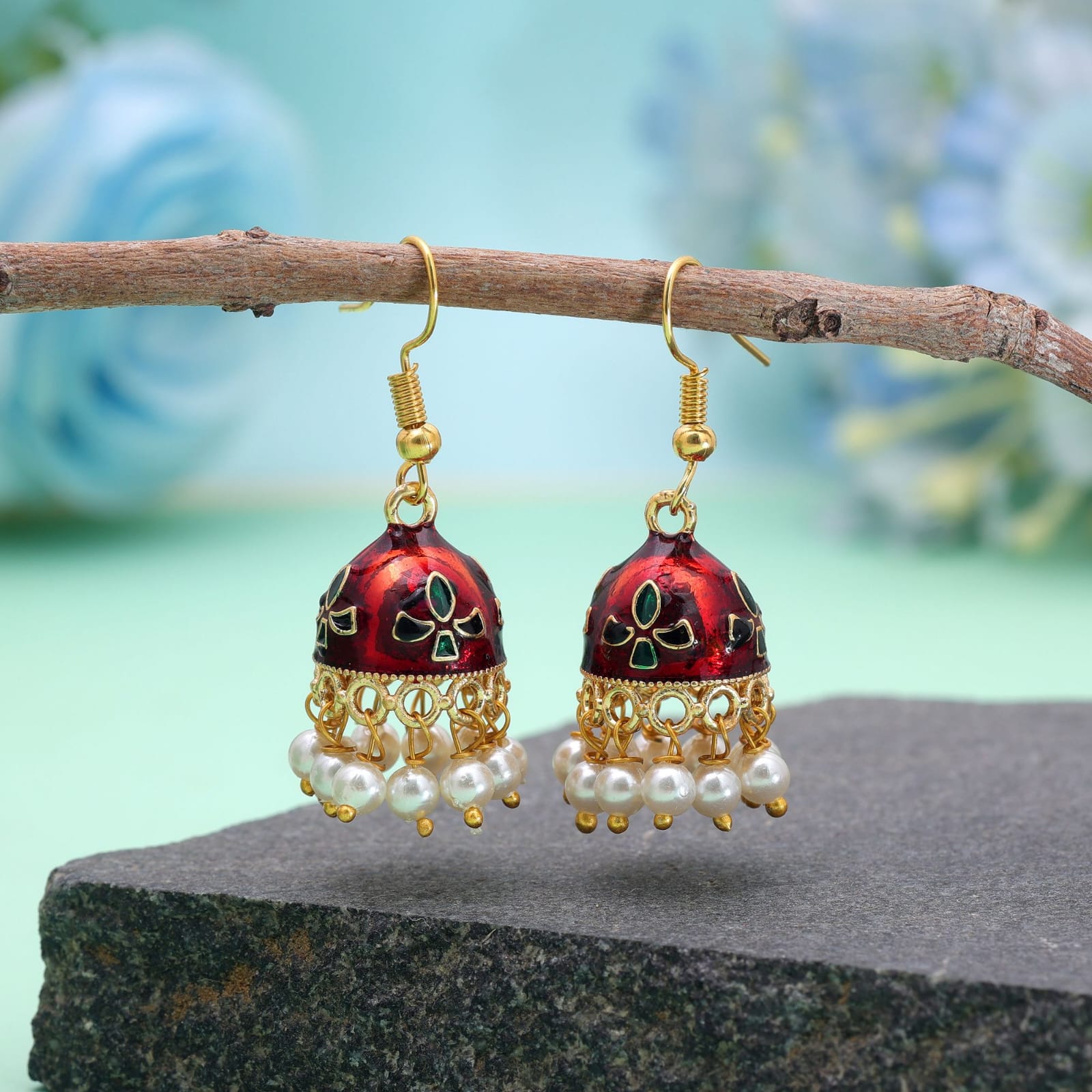 Bring subtle elegance to your wardrobe with these maroon Meenakari jhumka earrings, designed for both daily wear and special occasions. Crafted with a lightweight gold-toned frame, the compact bell-shaped domes feature smooth white enamelwork detailed with delicate red and green accents. A dainty rim of hanging white pearl beads adds soft charm and graceful movement. Styled with easy fish-hook earwires for all-day comfort, these versatile jhumkas pair effortlessly with everyday kurtas, casual fusion wear, or festive outfit ensembles.