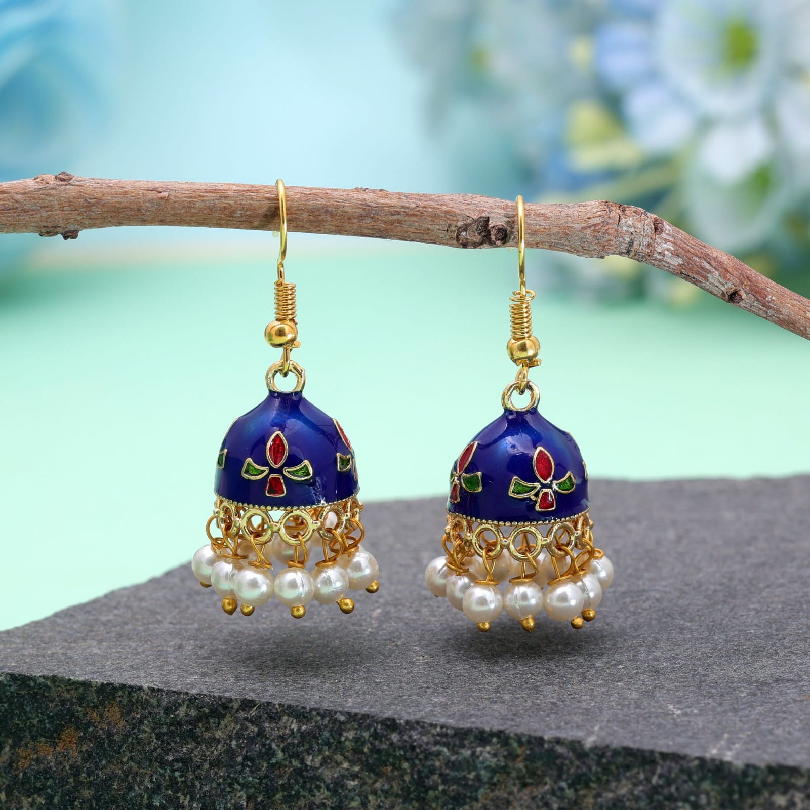 Bring subtle elegance to your wardrobe with these Blue Meenakari jhumka earrings, designed for both daily wear and special occasions. Crafted with a lightweight gold-toned frame, the compact bell-shaped domes feature smooth white enamelwork detailed with delicate red and green accents. A dainty rim of hanging white pearl beads adds soft charm and graceful movement. Styled with easy fish-hook earwires for all-day comfort, these versatile jhumkas pair effortlessly with everyday kurtas, casual fusion wear, or festive outfit ensembles.