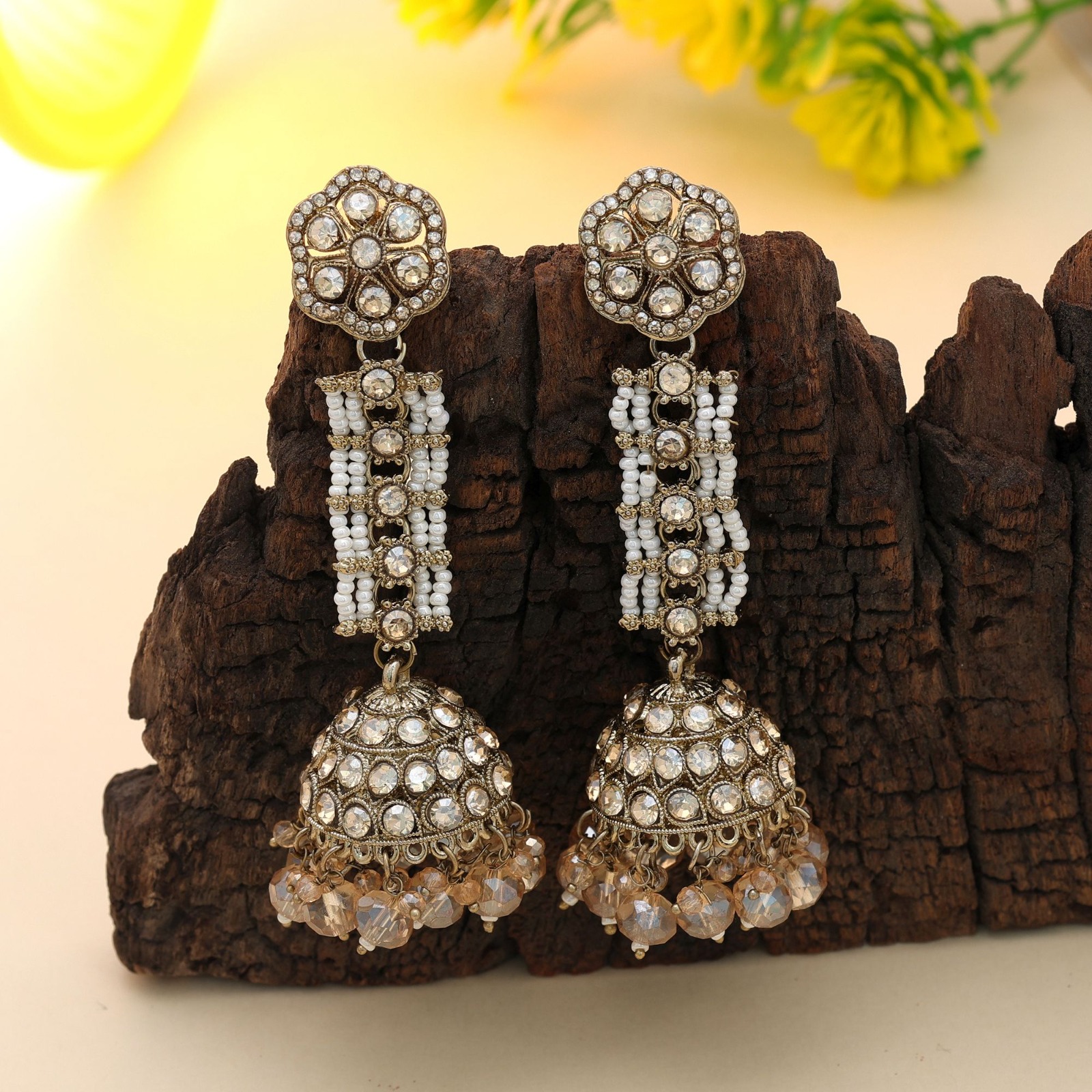 Antiqued gold statement jhumka earrings featuring a floral stud, white beaded multi-strand bridge, and crystal-studded dome with dangling champagne beads