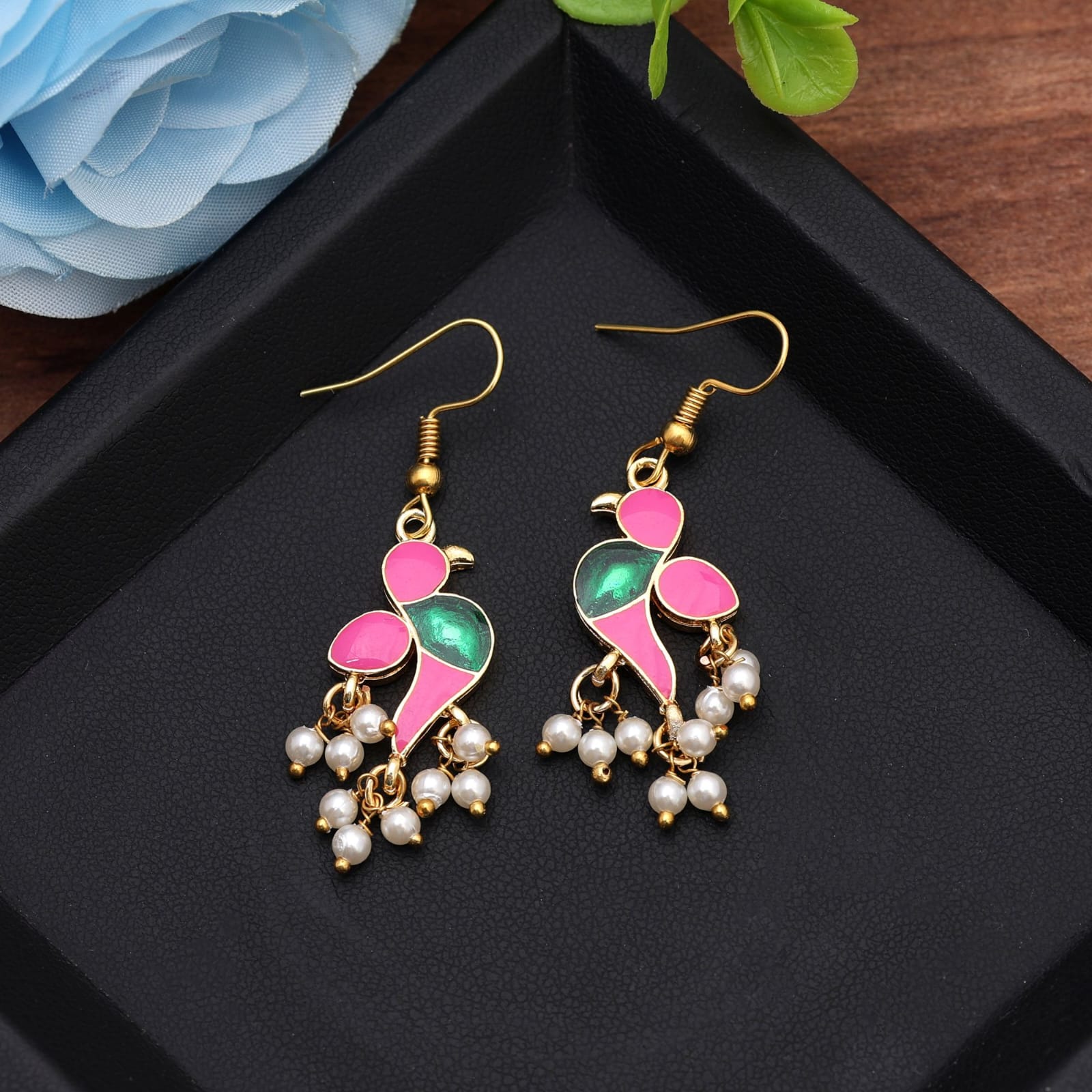 Elevate your ensemble with these handcrafted pink and green bird dangle earrings. Designed in a striking bright pink and shimmering emerald green enamel finish on gold-plated metal, each earring features a stylized bird silhouette accented with delicate clusters of small white pearl drops at the base. Fitted with comfortable fish-hook ear wires, these lightweight drop earrings add a playful yet elegant pop of color to ethnic wear, festive outfits, or modern fusion attire.