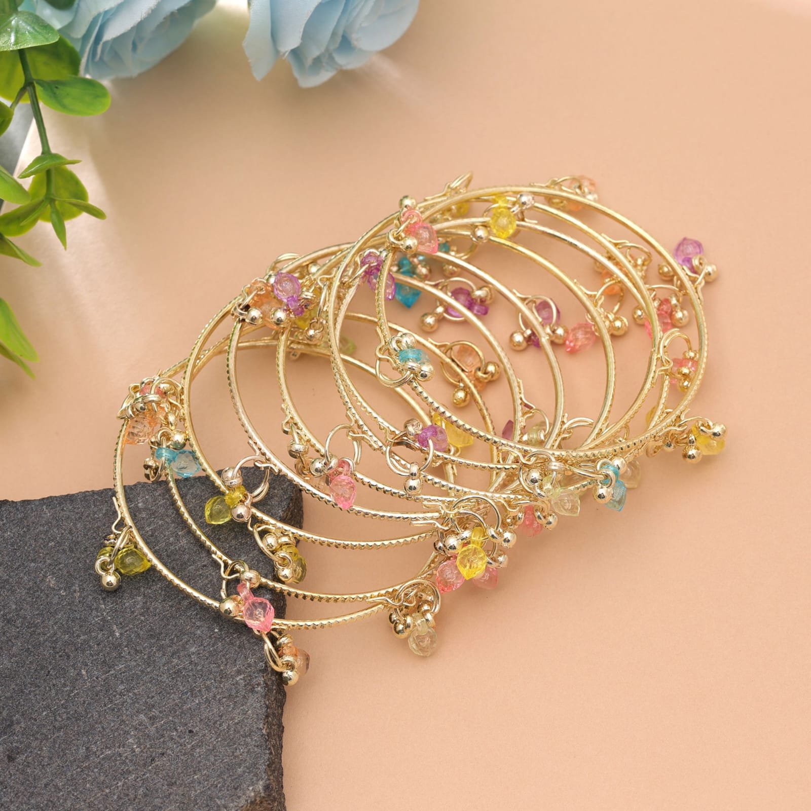 Set of slim gold-plated bangles decorated with colorful pastel crystal charms and small metallic ghungroo droplets.